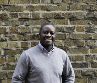 Headshot of Johah Muduhwe, Irish Refugee Council Finance and Administration Manager standing in front of a brick wall